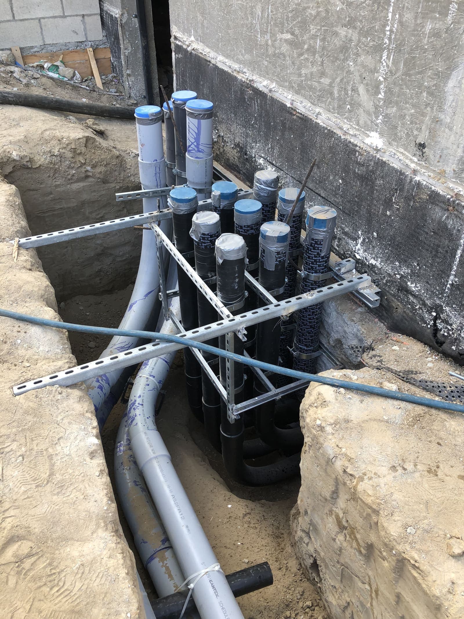 Stub-up bank of underground conduits emerging from a trench at a foundation