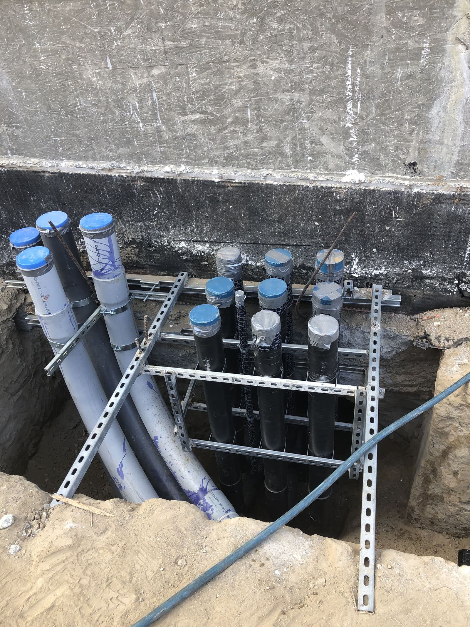 Multiple PVC and metallic conduit stub-ups at a service entrance trench