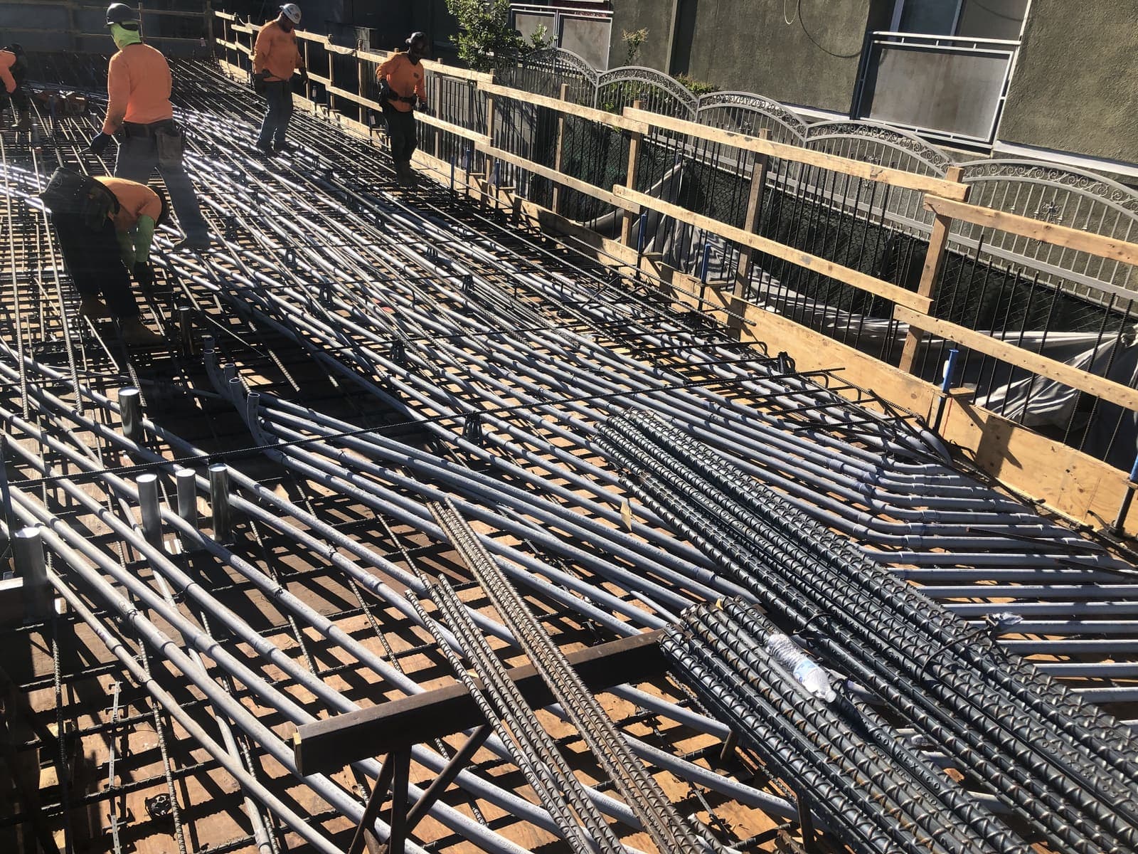 Workers walking a rebar deck with conduit roughed in before a concrete pour